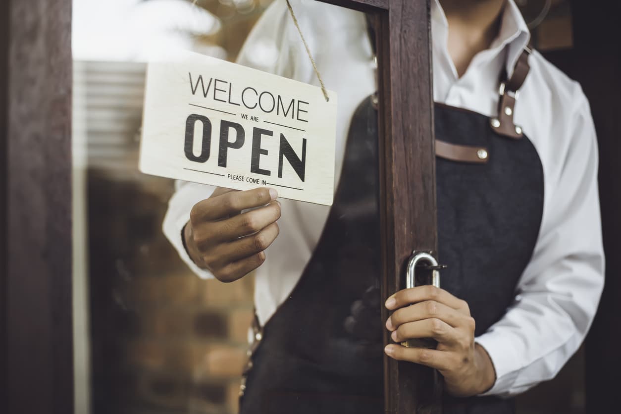A store owner turns the sign on his front door to read “Welcome, we are open, please come in.”
