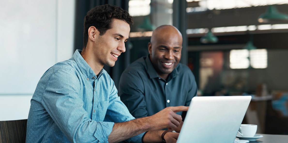 a photo of a two man sitting at a table using a laptop computer