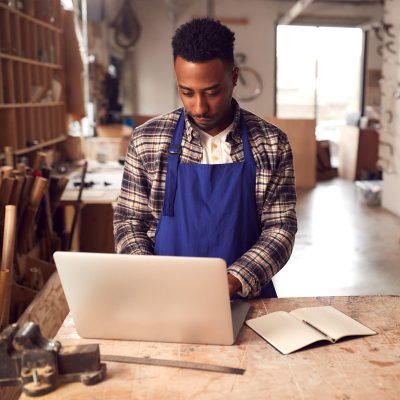 A Person Standing At A Table Using A Laptop