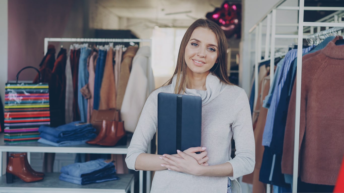 A woman stands proudly in a clothing store franchise holding a tablet.